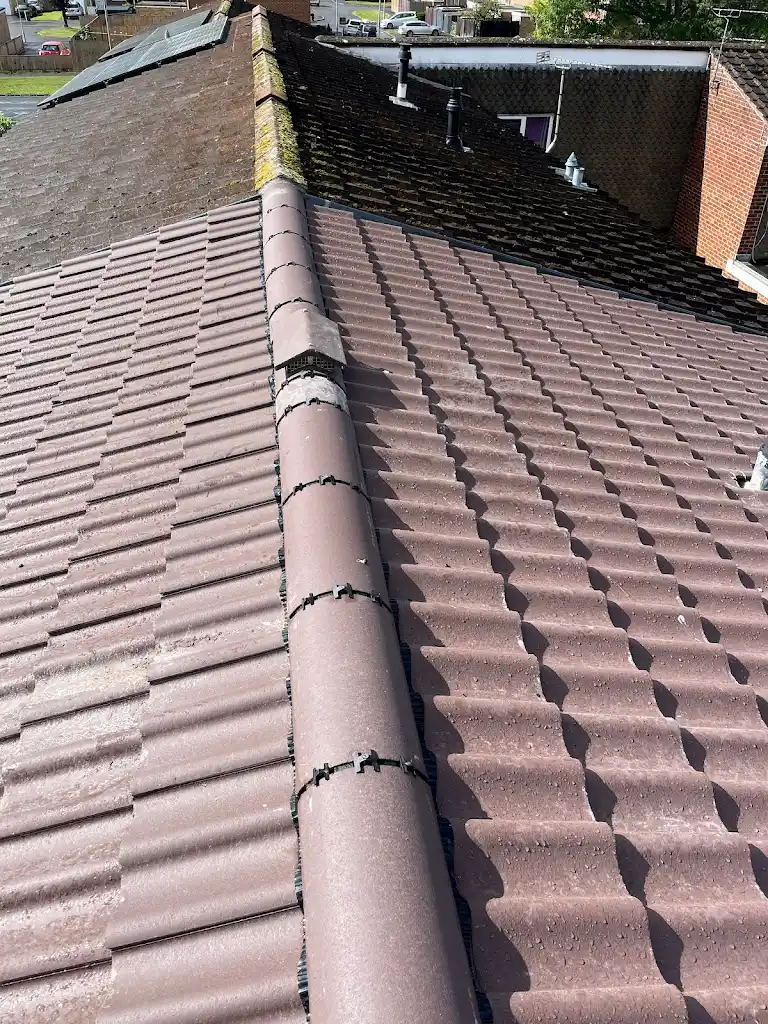 A roof showing a clear division between two sections. The left side is covered with weathered, dark shingles, while the right side features newer, clean, light brown tiles. The ridgeline separates the contrasting roofing styles.