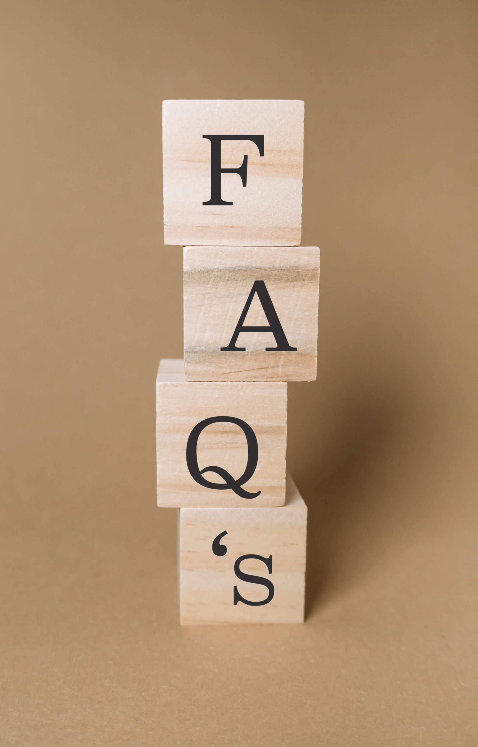 Four wooden blocks are stacked vertically, each with a large black letter printed on its face. From top to bottom, the blocks spell out "F", "A", "Q", and "'s" against a plain beige background.