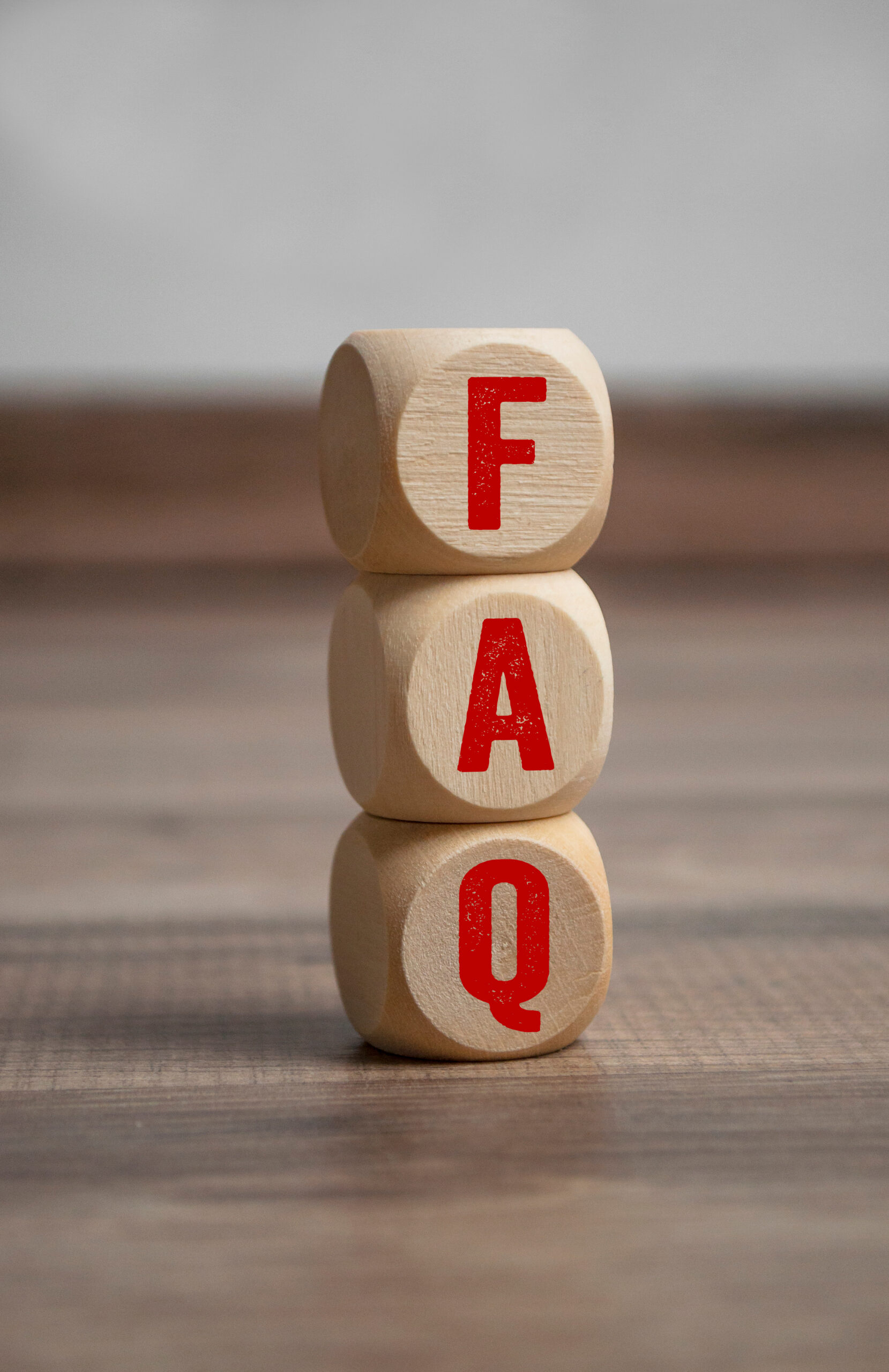 Three wooden blocks stacked vertically, each with a red letter spelling "FAQ" against a blurred wooden surface background.