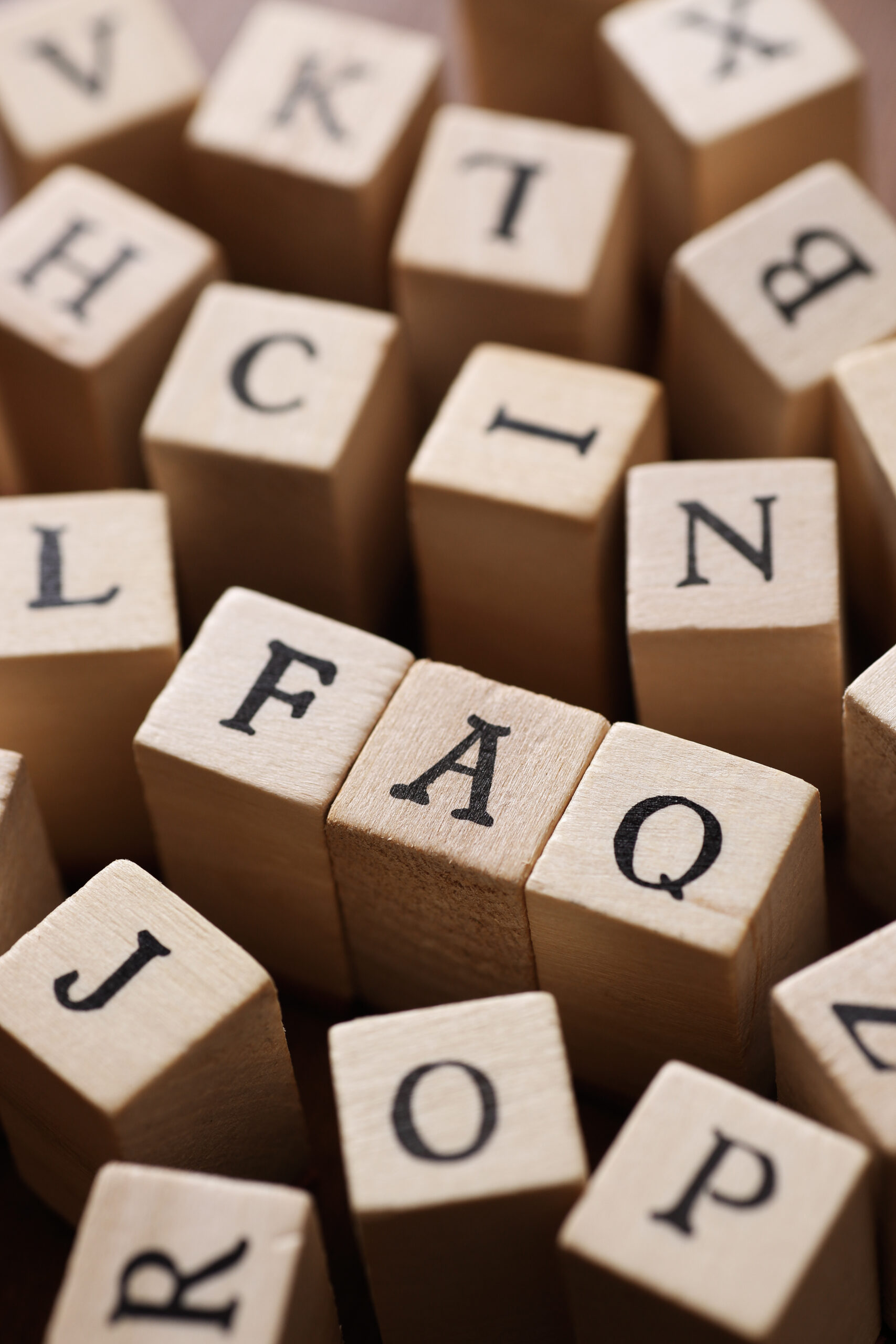 Several wooden blocks with black letters are arranged closely together. Three blocks in the center spell out "FAQ," surrounded by other random lettered blocks.
